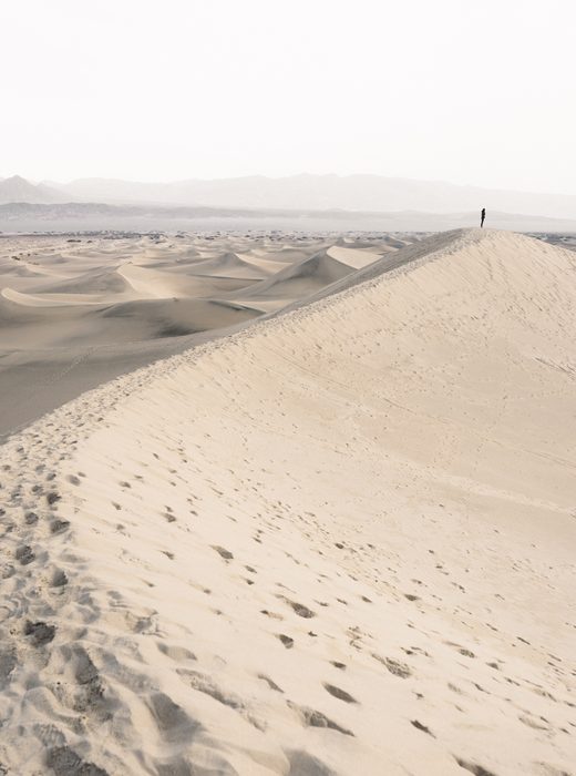 Pale sand dunes with footprints under a white sky