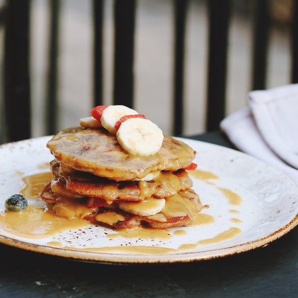 A stack of pancakes with banana slices and syrup on a white plate