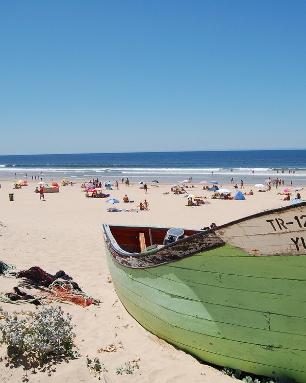 A green wooden fishing boat on a sunny beach by the ocean