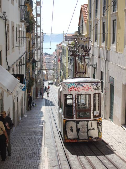 An old yellow tram climbing a narrow Lisbon street