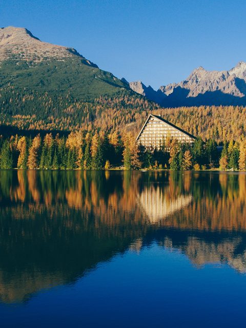 Autumn larch forest and a hotel reflected in a calm mountain lake