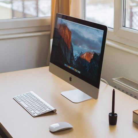 White desk with a computer, keyboard and pen holder by a window