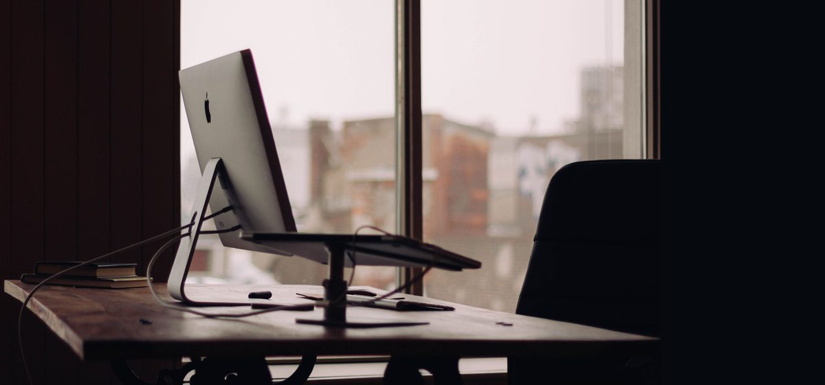 Dark desk with a computer facing a tall window