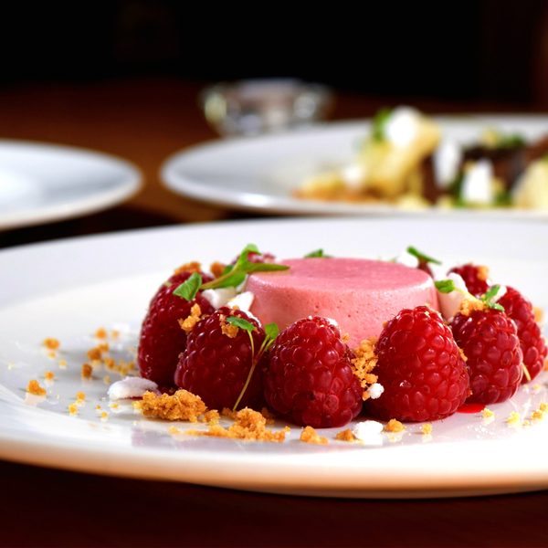 Pink panna cotta with fresh raspberries and crumble on a white plate