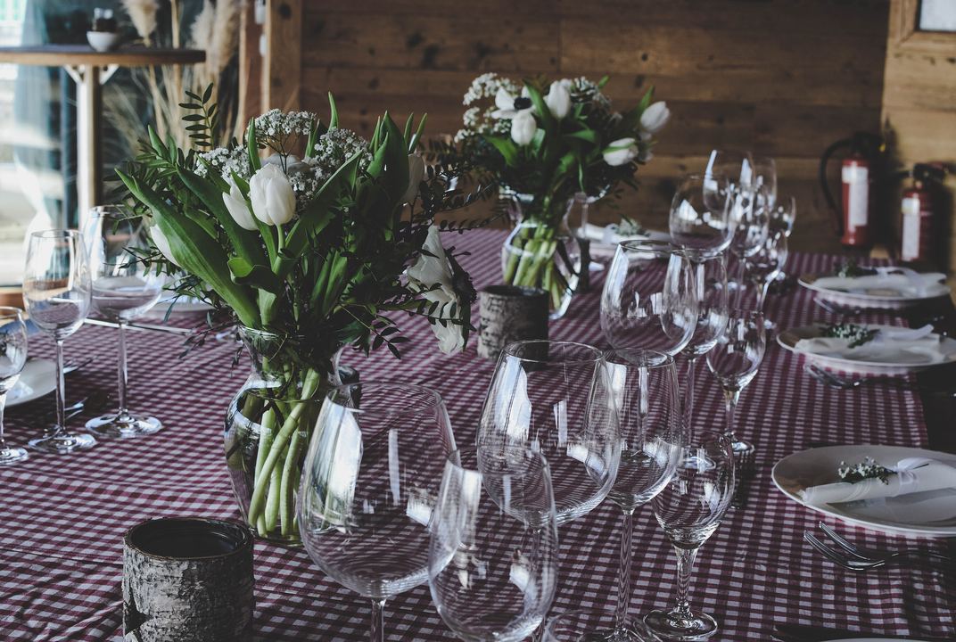 A long dinner table set with wine glasses, white tulips and a plum checked cloth