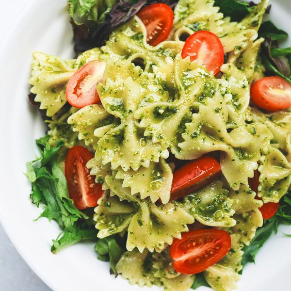 Bow tie pasta with green pesto and cherry tomatoes in a white bowl