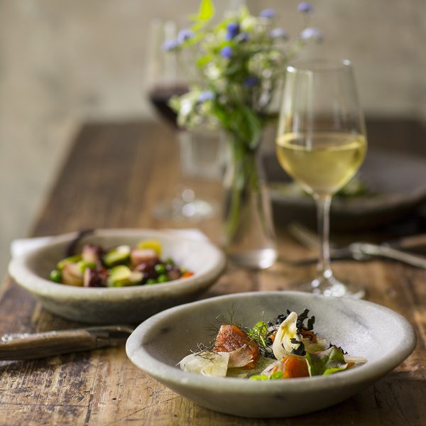 Two small plates of salad beside a glass of white wine on a rustic table