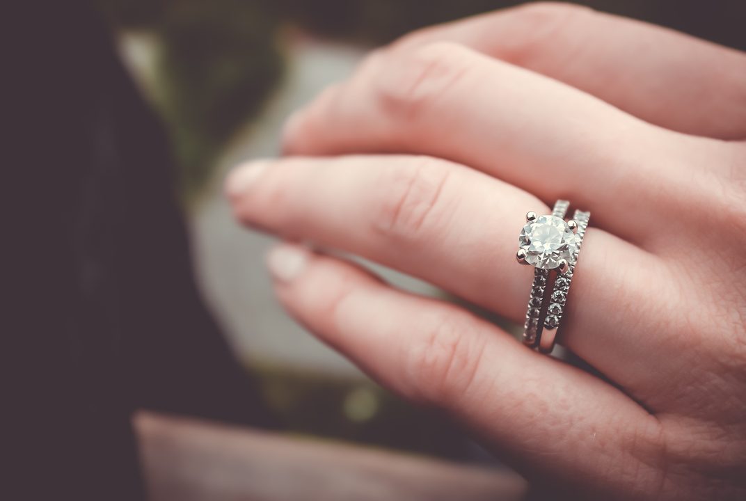 A diamond engagement ring with a slim pave band on a woman's hand