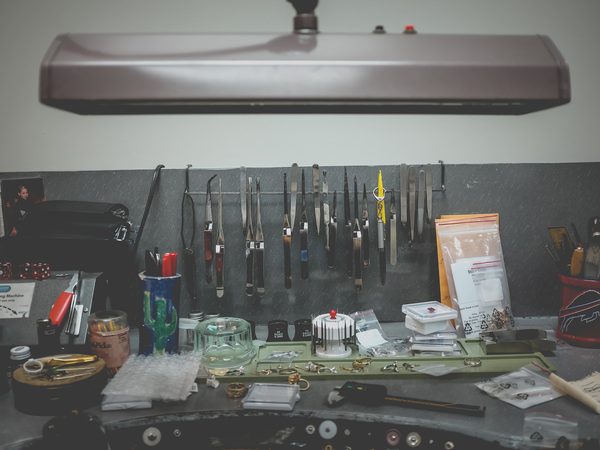 A jeweler's workbench with pliers and tweezers on a rail under a lamp