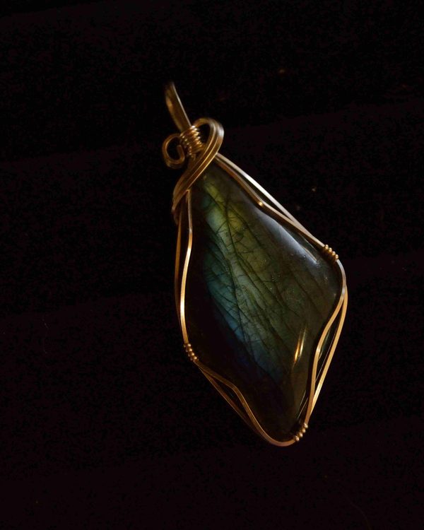 A labradorite stone wrapped in gold wire on a black background