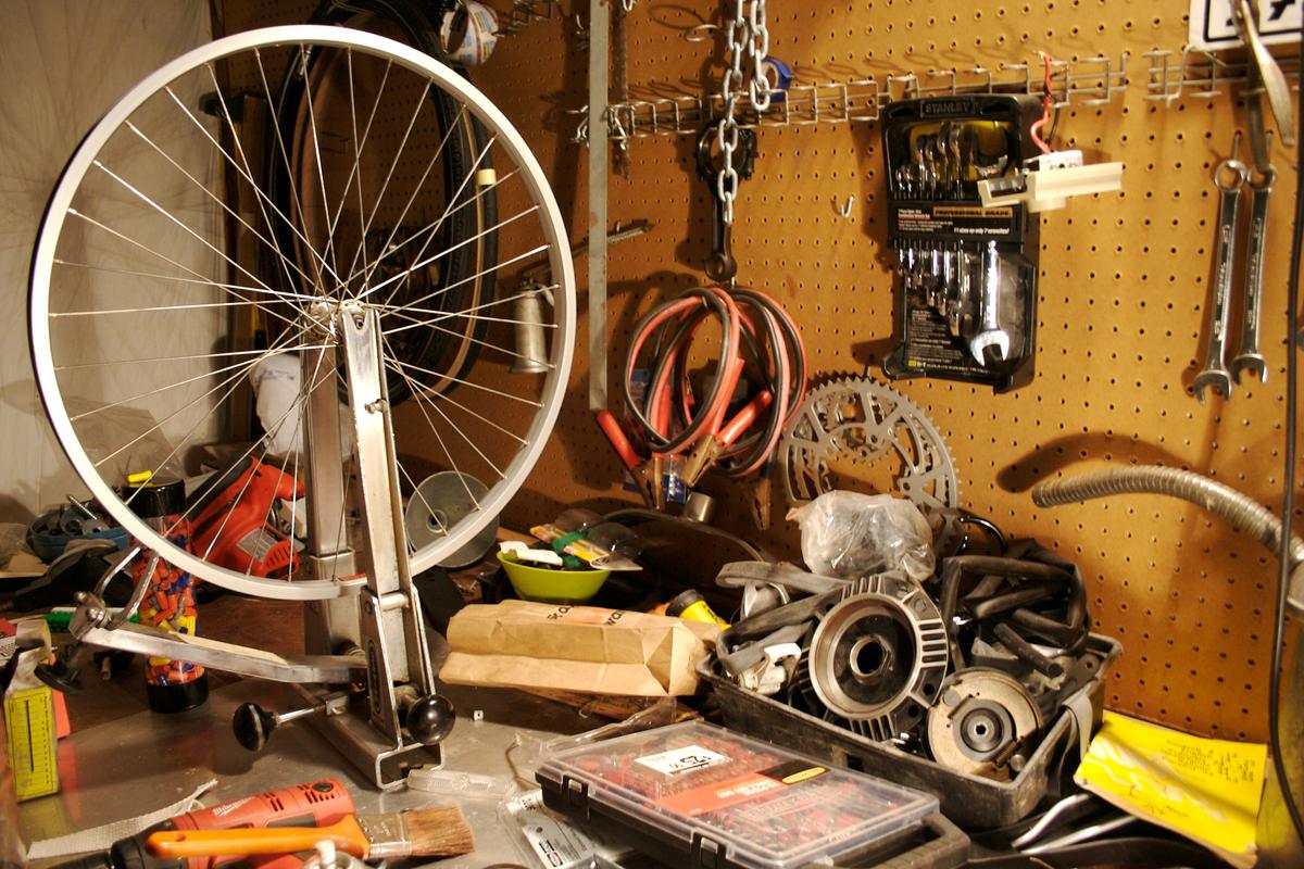 Bicycle wheel in a truing stand on a workbench, with tools on a pegboard behind