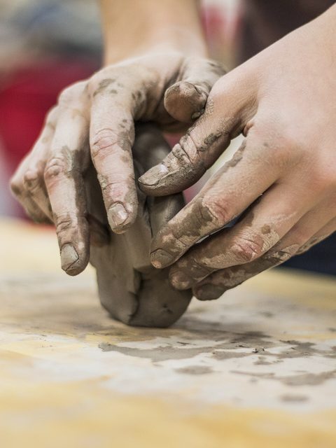 Hands kneading a lump of clay on a wooden work table