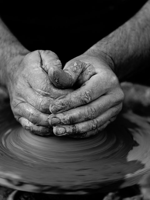 Strong hands centering a mound of clay on a wheel