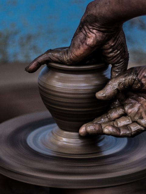Muddy hands raising the walls of a small pot on a wheel