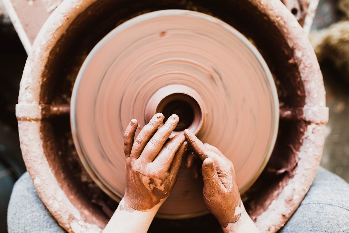 Two hands shaping terracotta clay on a spinning potter's wheel