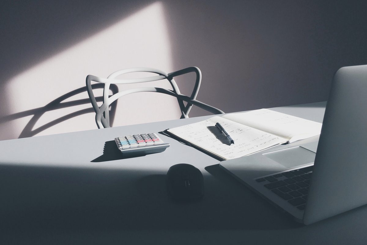 A laptop and notebook on a grey desk in soft window light