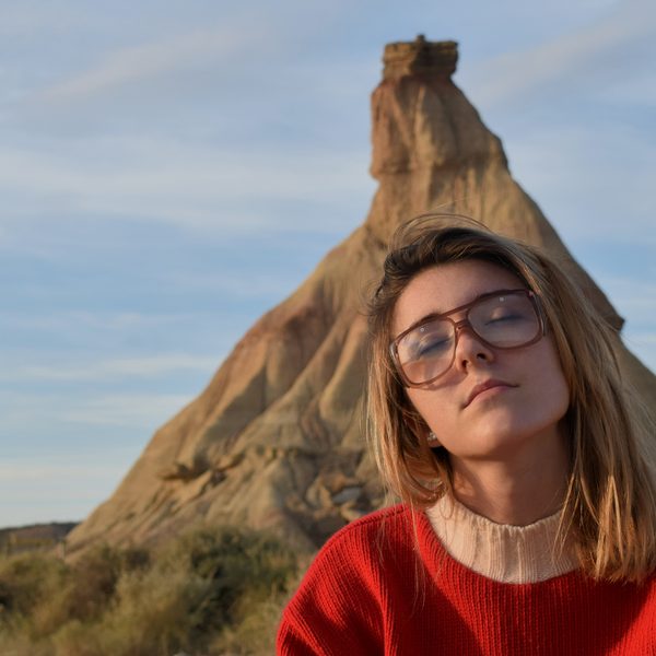 Woman in a red knit sweater and round glasses in front of a desert rock