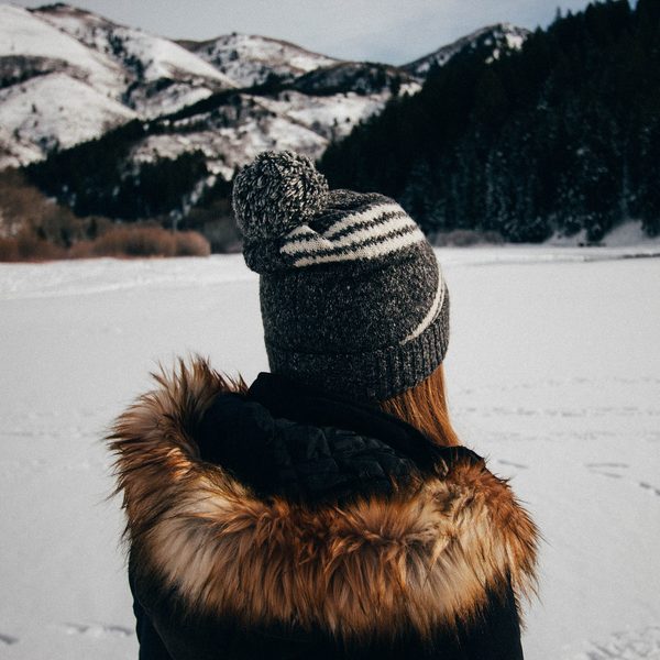 Dark parka with a fur trimmed hood and a striped knit hat in the snow