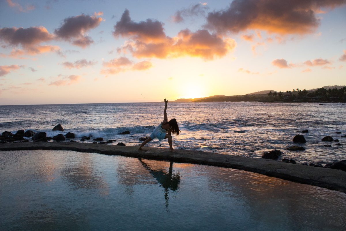 A person doing a yoga pose at the edge of a tidal pool at sunrise