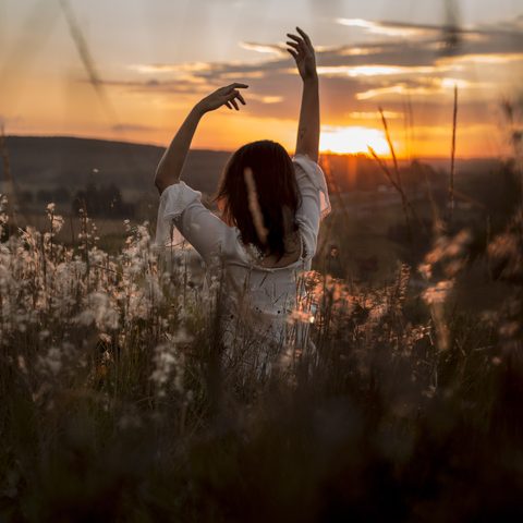 A woman stretching her arms in a field of tall grass at sunset