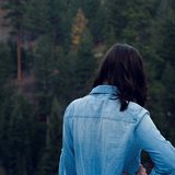 Woman in a light denim jacket seen from behind in a forest