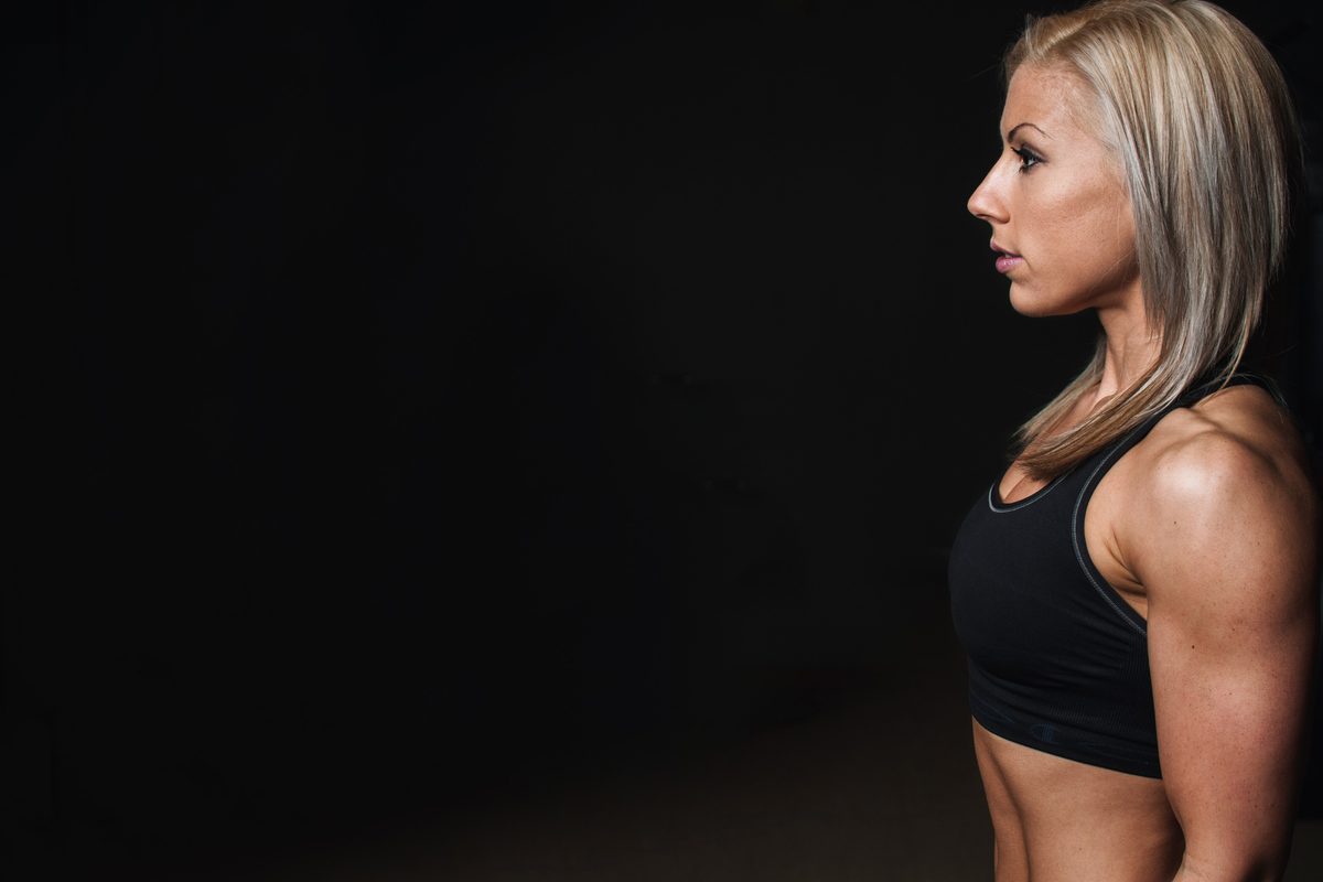 An athlete in a black sports top stands in profile in a dark gym