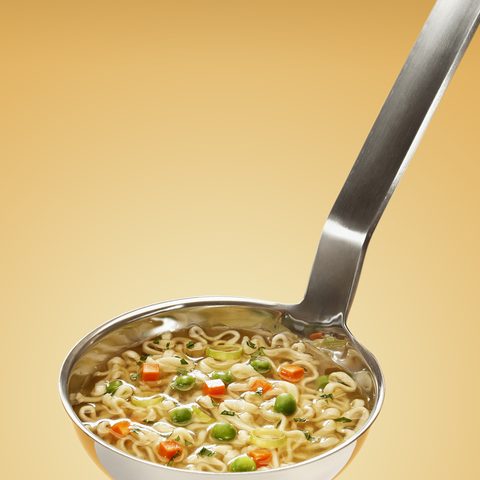 A ladle full of noodle soup with carrots and peas
