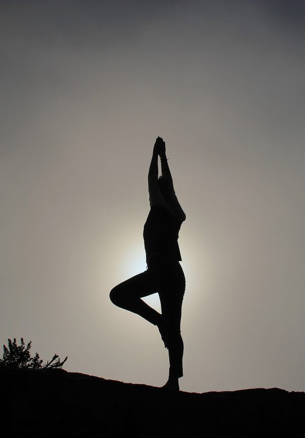 A person holds a tree pose on a hilltop in soft gray morning mist